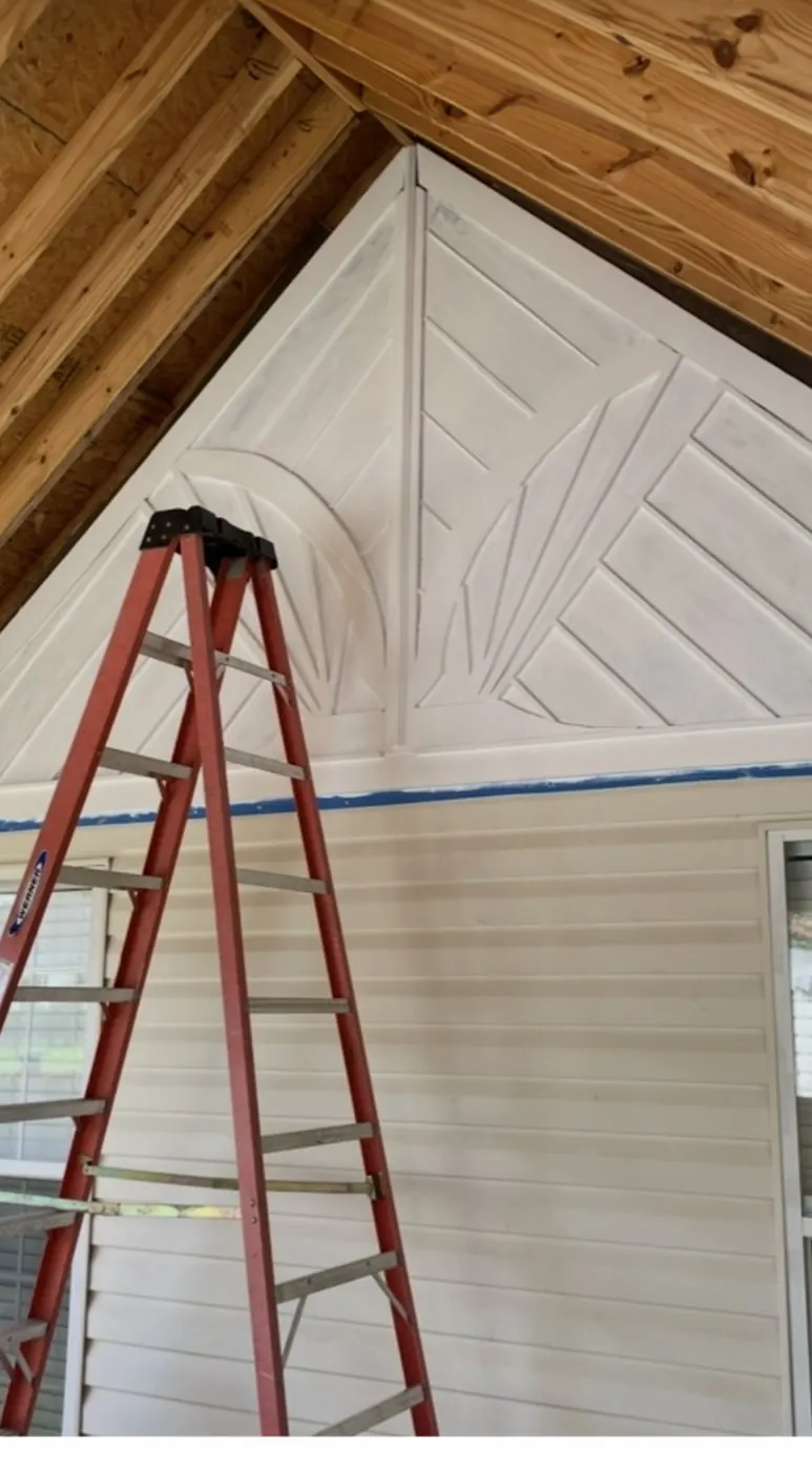 White geometric panel work filling a gable above a covered porch, in progress