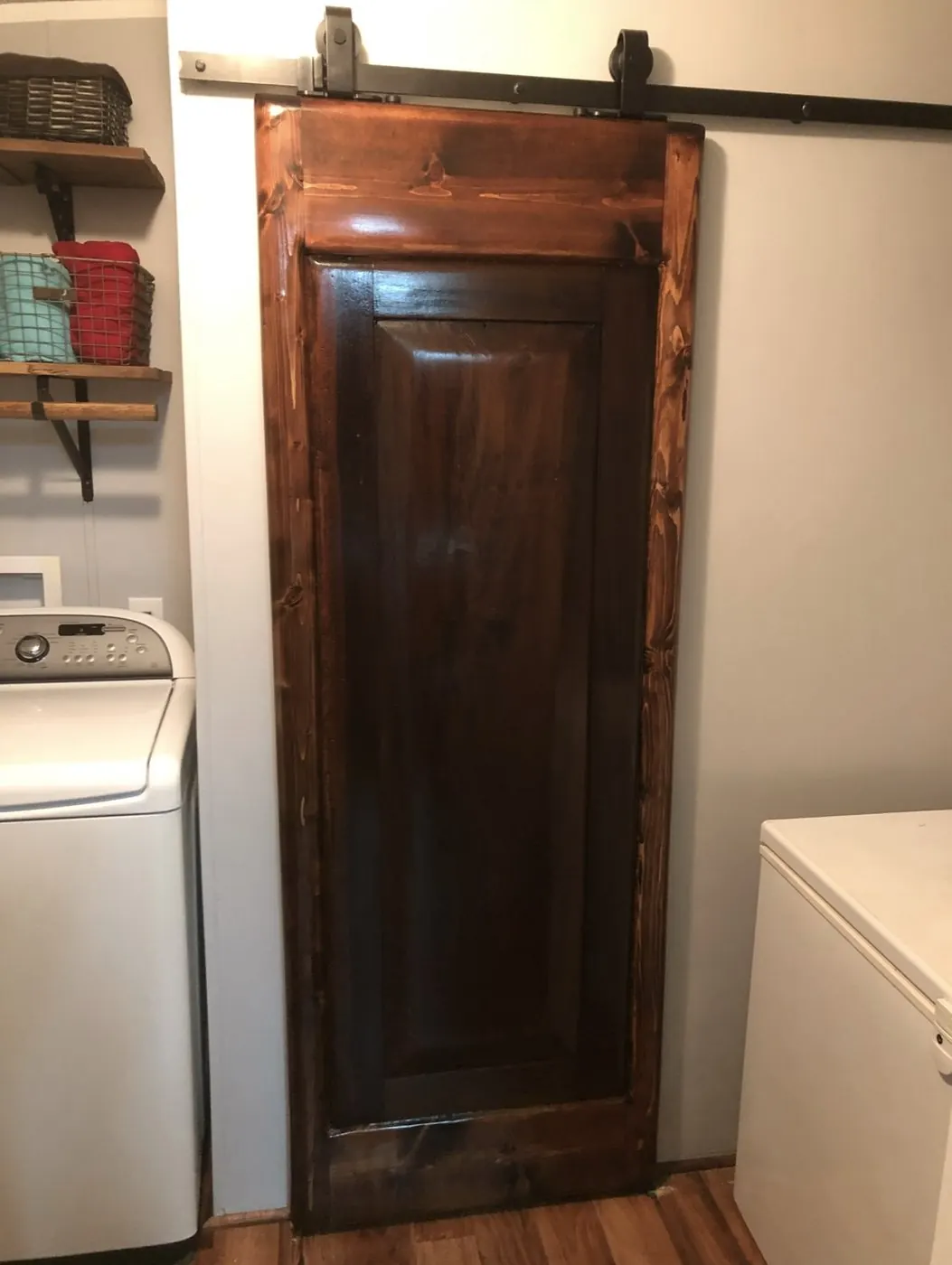 The finished barn door hung on a black rail between the washer and dryer