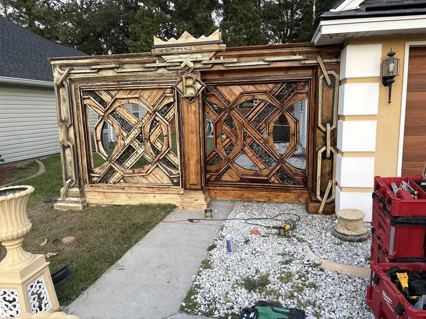 Gate mid-staining, right panel stained and left panel in progress, with carved crown and brass B