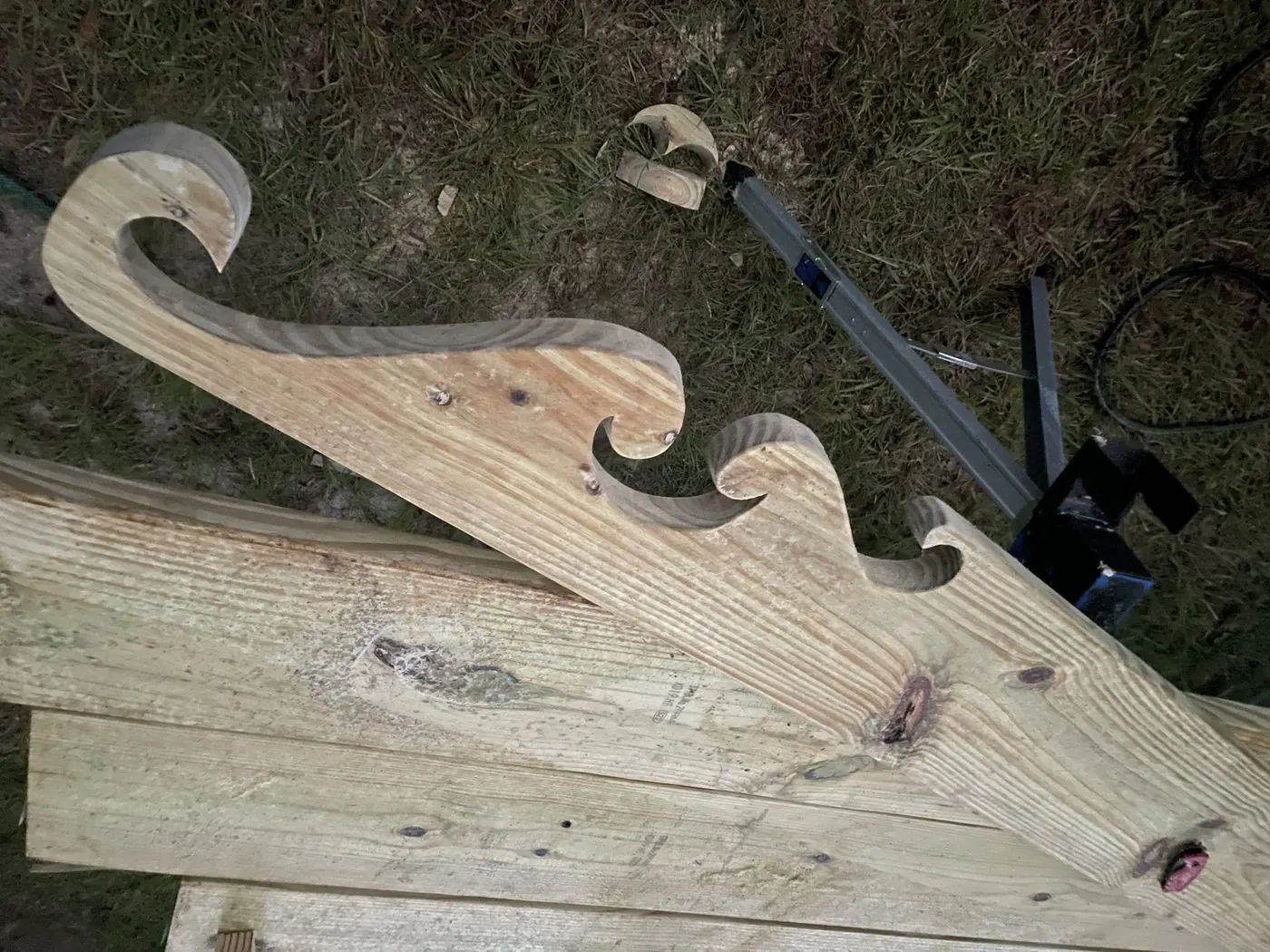 Carved wave-pattern rafter tail lying on stacked lumber at night