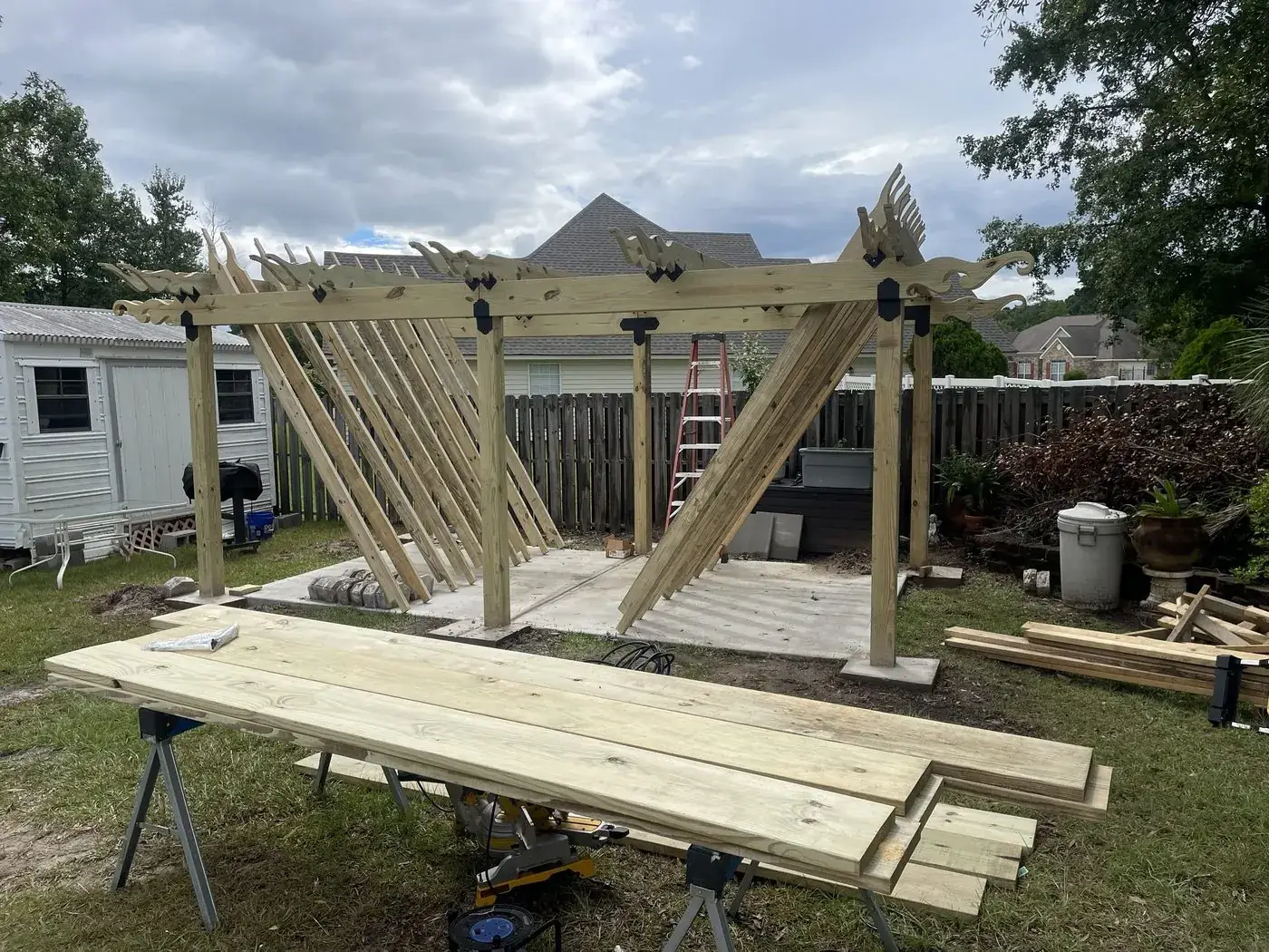 Pergola posts and carved beams standing, rafters leaning against the frame