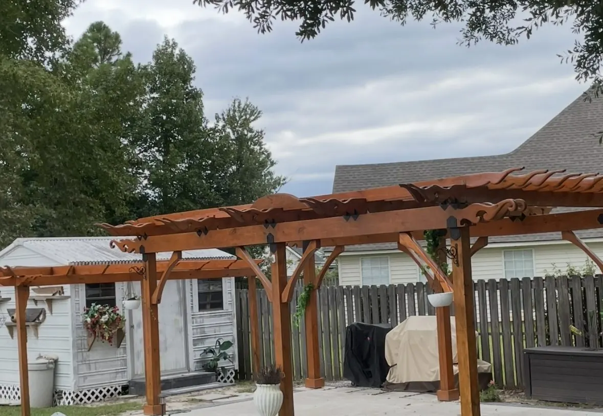 Stained timber pergola with carved scroll rafter tails over a patio
