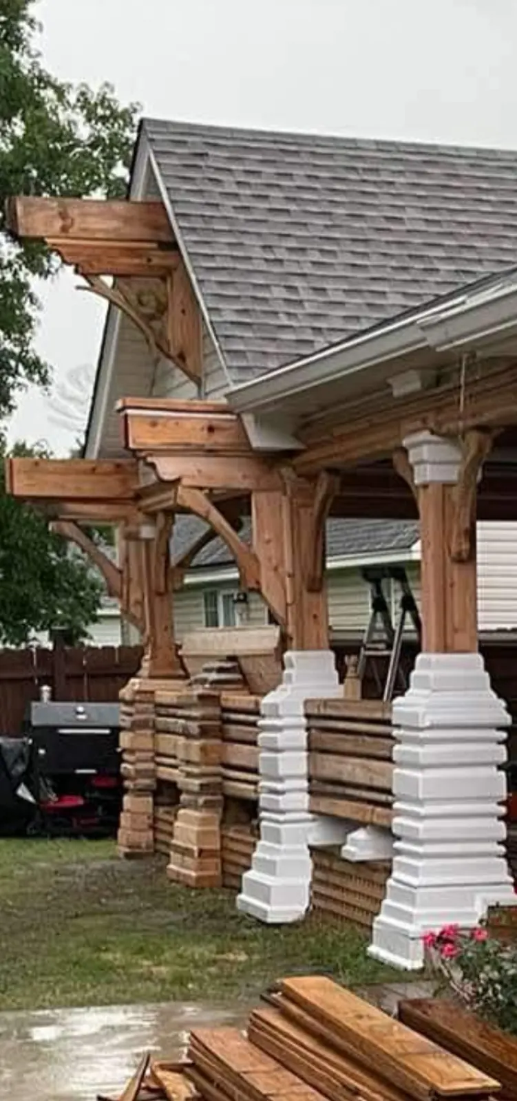 Covered porch framed in heavy timber with carved corbels and stepped white post bases, under construction