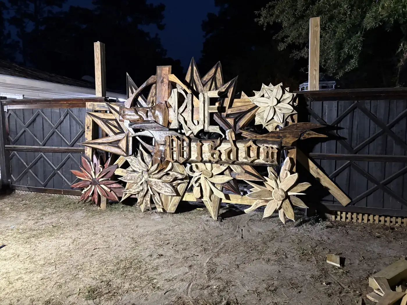 Large carved TRUE WISDOM sign with wooden florals, lit at night