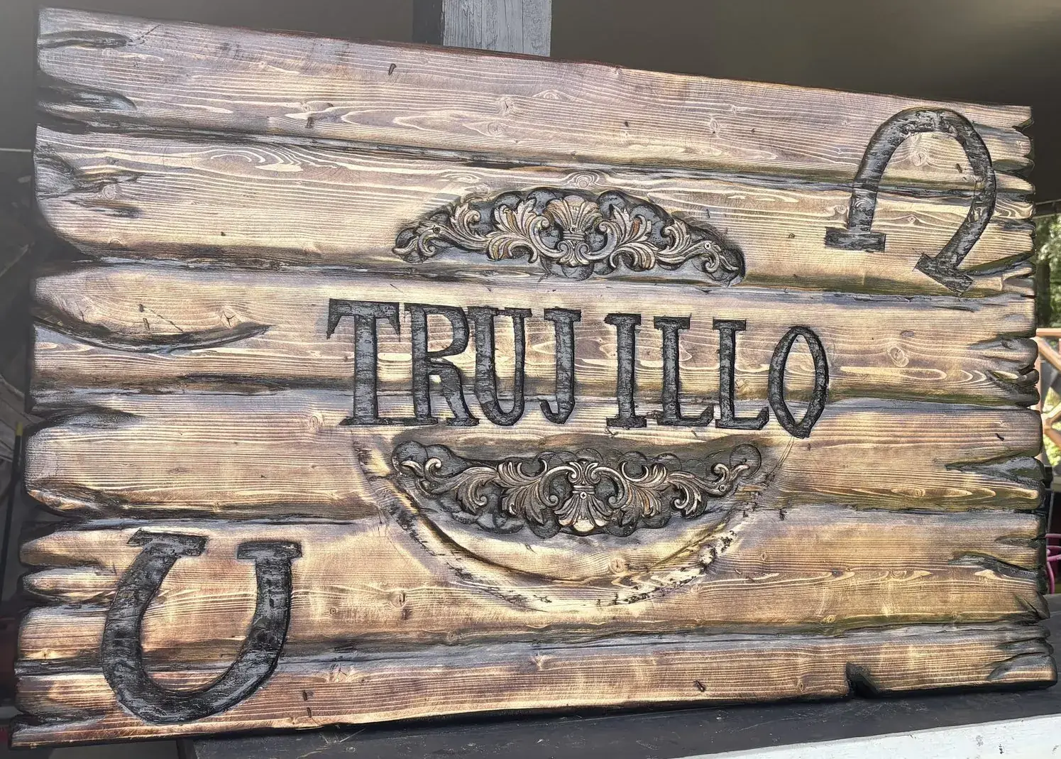 Carved family name sign with horseshoes and scrollwork on burned pine